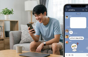 วิธีส่งข้อความว่างใน LINE แกล้งเพื่อนง่ายๆ ด้วยเทคนิคข้อความล่องหน ภาพ split-screen: ทางด้านซ้าย ผู้ชายชาวเอเชียอายุน้อยนั่งอยู่บนโซฟาสีเทาในห้องนั่งเล่นที่สว่างไสว กำลังยิ้มและหัวเราะขณะมองลงมาที่สมาร์ทโฟนในมือของเขา ทางด้านขวา มีส่วนแทรกหน้าจอสมาร์ทโฟนขนาดใหญ่